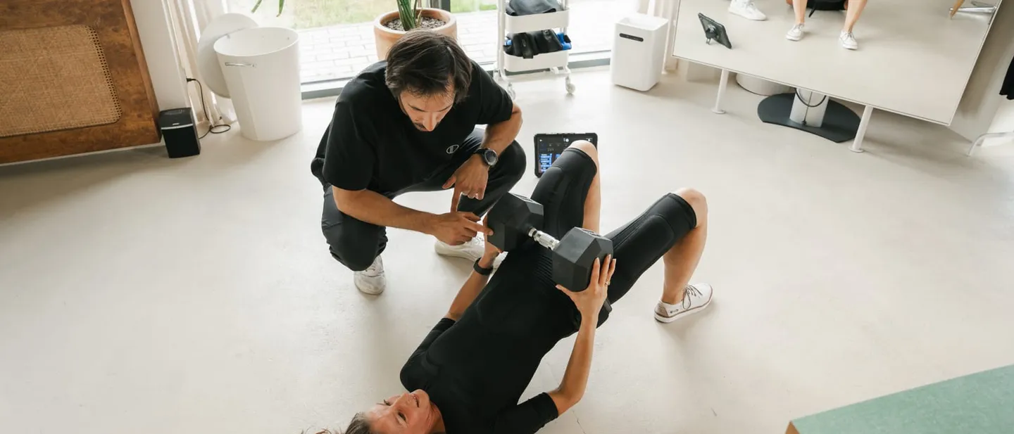 A coach assisting a client exercising with a dumbbell on a mat at the WorkItEMS studio