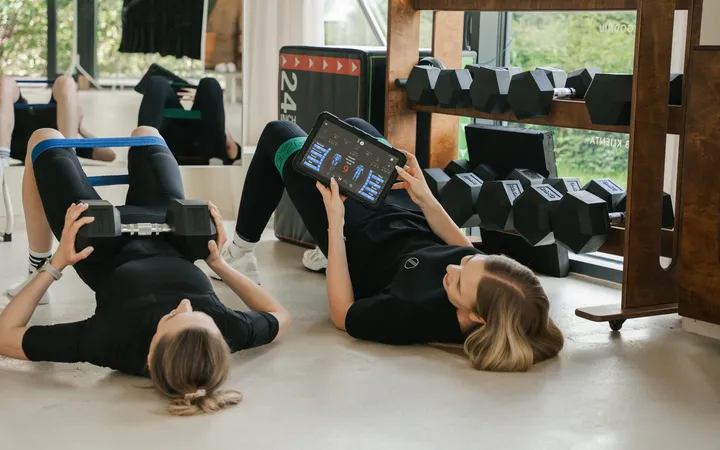 Two people training on mats at the WorkItEMS studio, the coach showing an exercise on a tablet