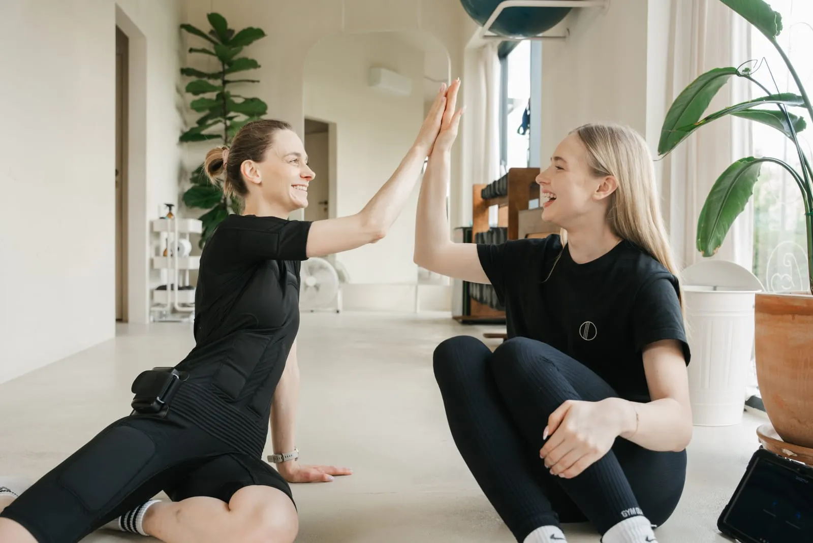 A client in an EMS suit and her coach high-five after a session