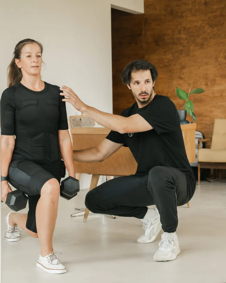 A coach correcting a client's position in an EMS suit during a session in the studio