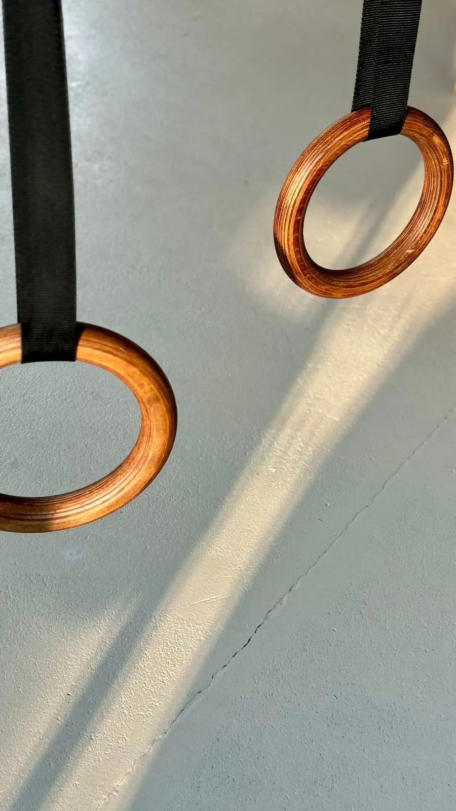 Wooden gymnastic rings on black straps, in a shaft of light on the wall