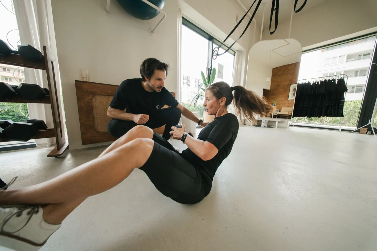 A coach guiding a client in an EMS suit through a core exercise on the mat