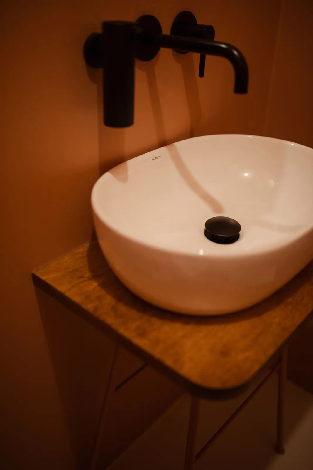 An oval basin on a wooden countertop with a black wall-mounted tap