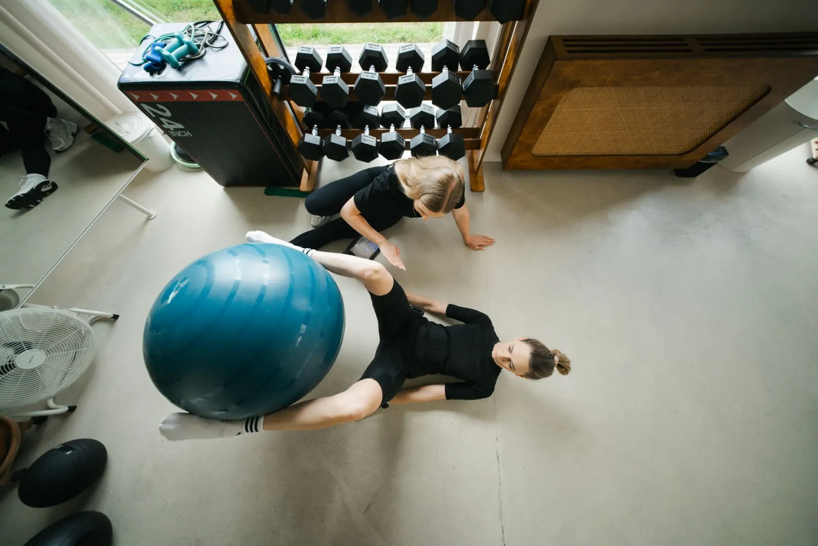 A client in an EMS suit training with a large exercise ball while lying on the mat