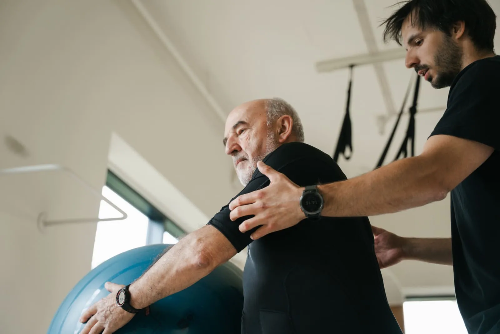 A coach correcting the arm position of a client leaning on an exercise ball