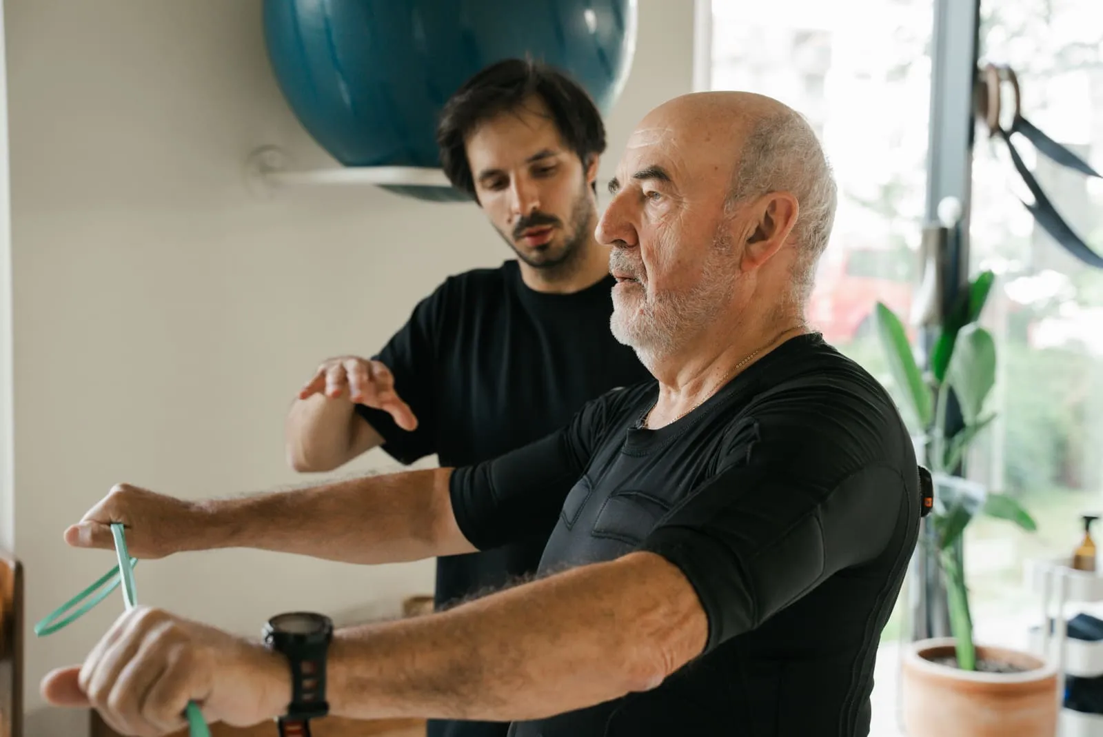 A resistance band exercise - the coach guiding a client in an EMS suit