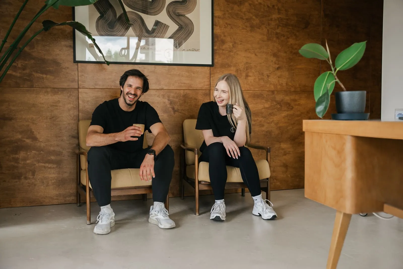 A coach and client resting in armchairs after a session by the wooden wall
