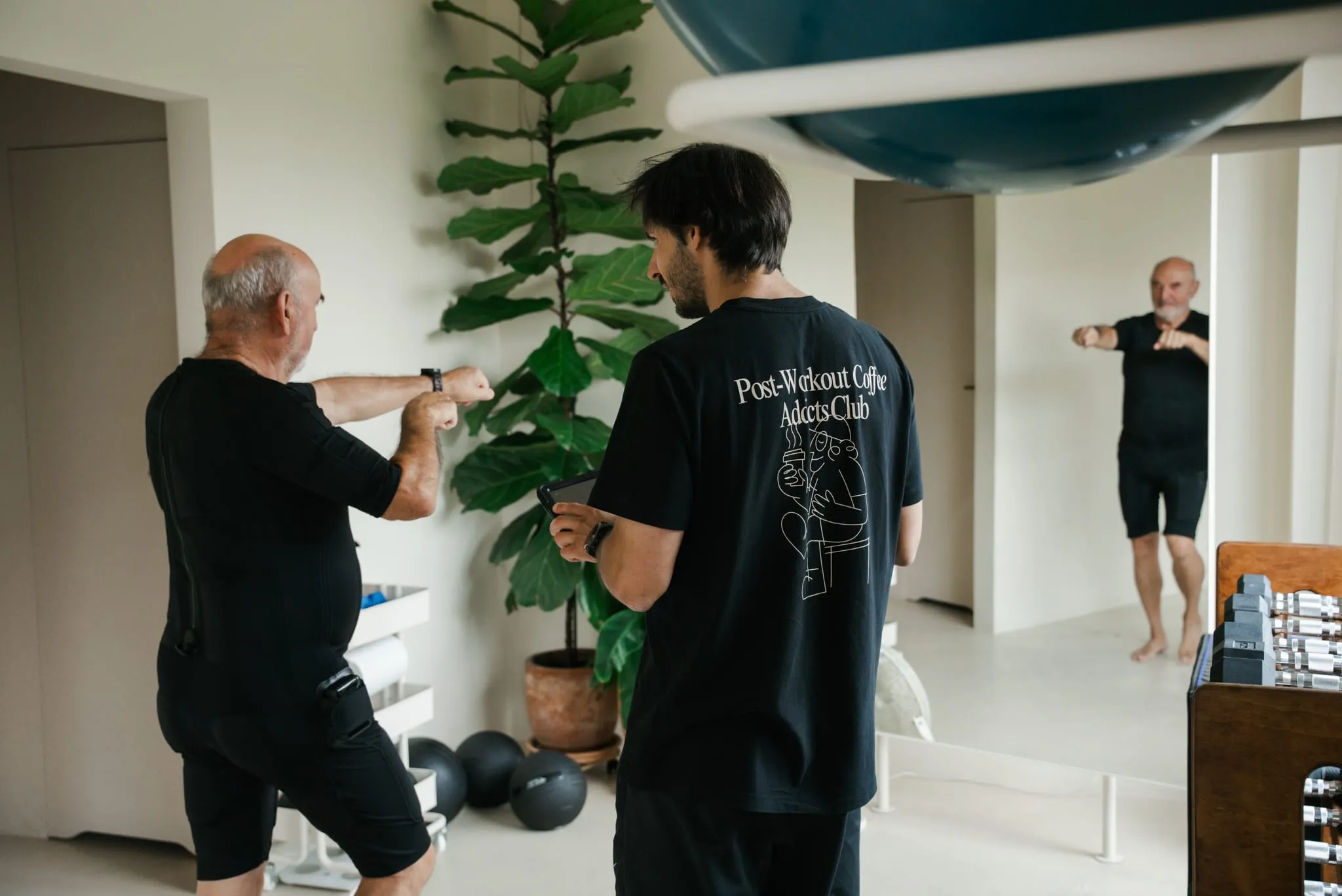 A coach in a WORK IT shirt guiding a client through a striking exercise beside the plant