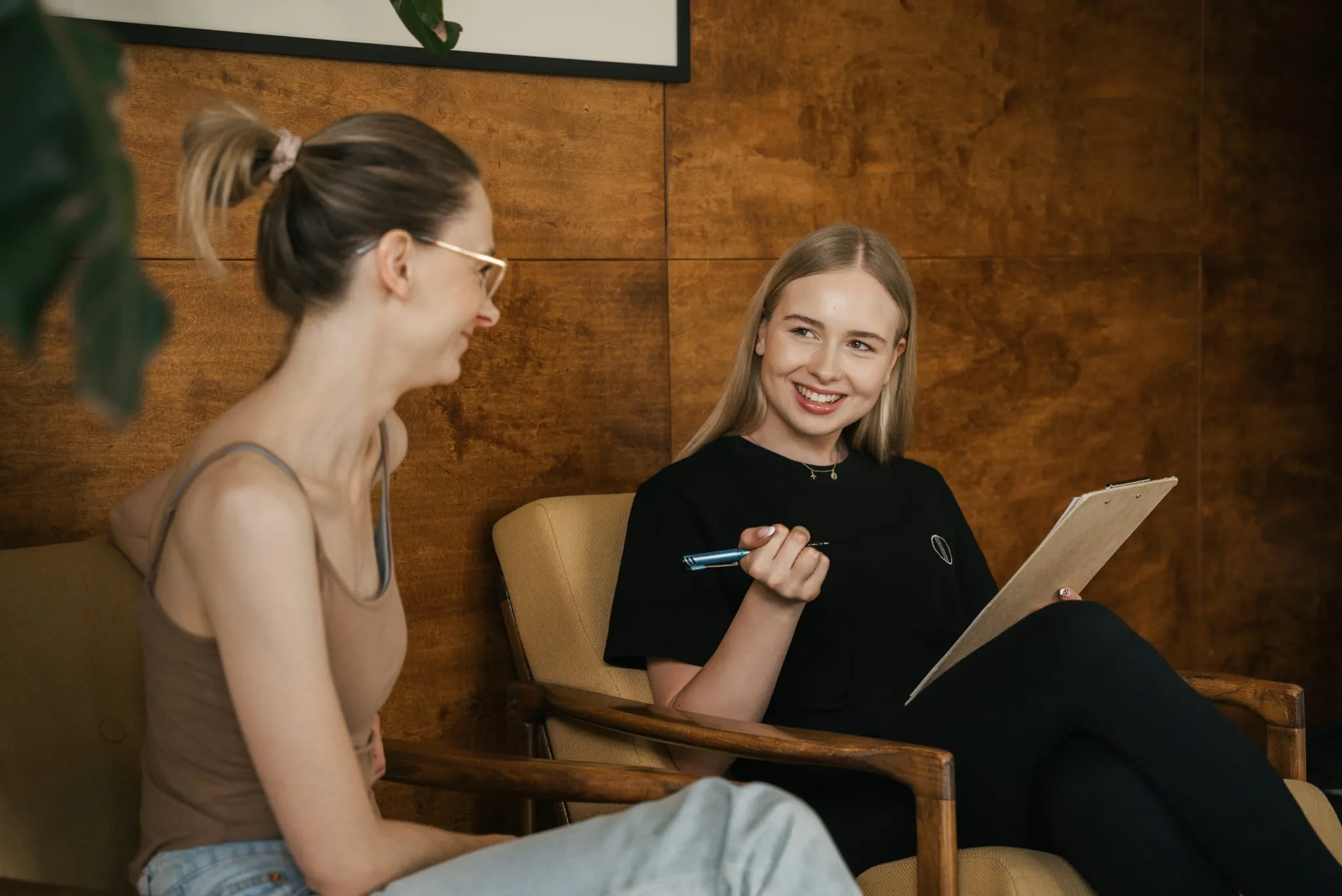 A coach with an intake form talking to a client in armchairs by the wooden wall