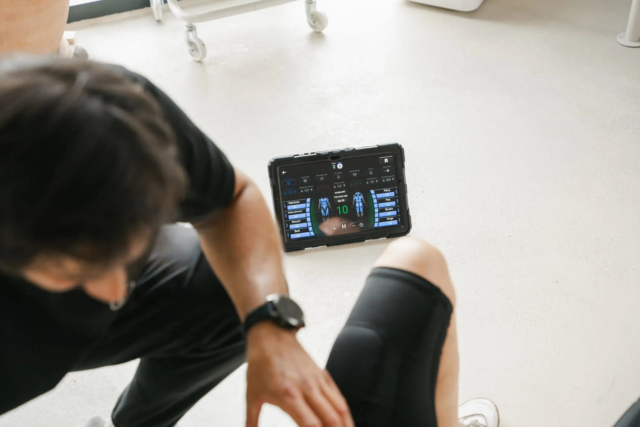 A tablet controlling the EMS device on the studio floor, the coach adjusting it