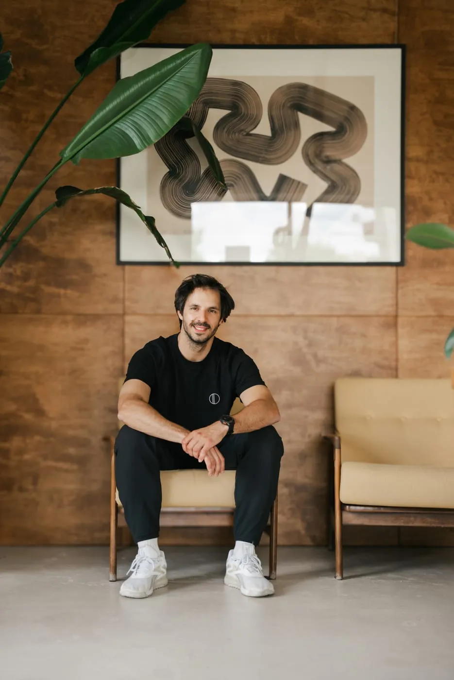 Łukasz, founder of WORK IT EMS, sitting in an armchair by the studio's wooden wall