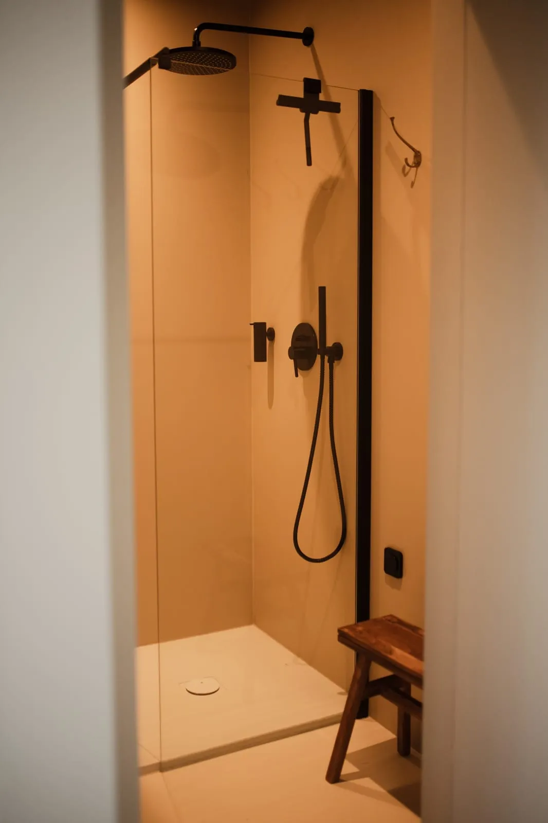 A shower with black fittings and a wooden stool in the studio bathroom